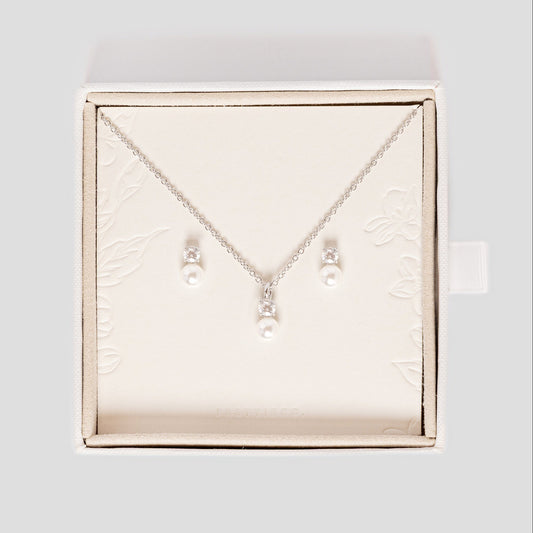 A silver necklace and matching stud earrings with small pearl-like beads, displayed inside an open cream-colored jewelry box on a light gray background. Perfect for wedding day bridal jewellery