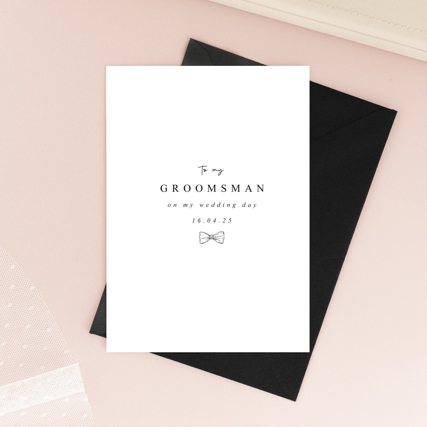 Folded A6 groomsmen card printed on textured white cardstock with a minimalist black bow tie illustration and elegant typography.
