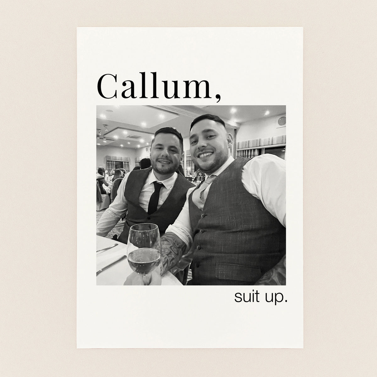 A personalized black and white wedding print featuring a photo of two men in suits, with the text 'Callum,' at the top and 'suit up.' at the bottom, displayed on a light beige background.