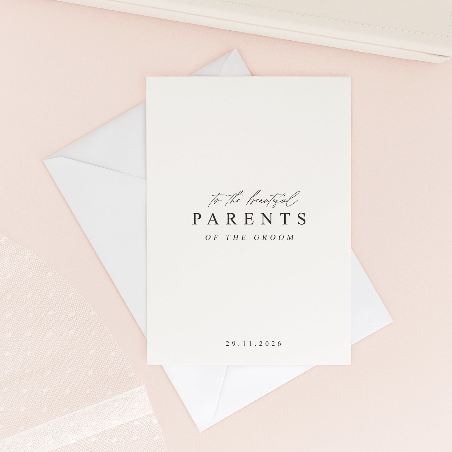 Elegant wedding card for the parents of the groom, featuring modern calligraphy and minimalist design, styled flat lay with white envelope on a blush background.