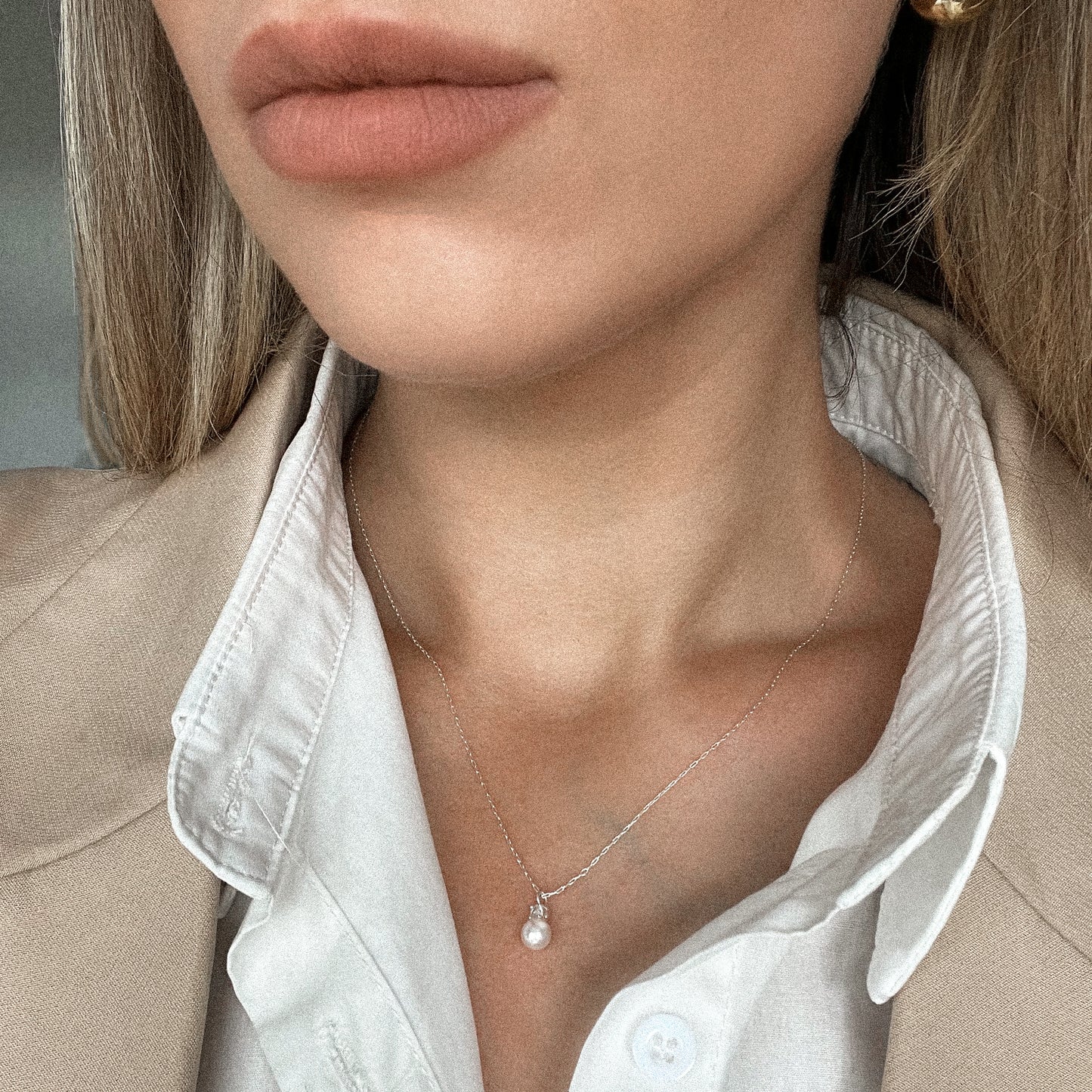 "Elegant pearl drop necklace on a woman wearing a white shirt and beige blazer. The delicate sterling silver chain holds a single lustrous pearl pendant, perfect for bridesmaids, weddings, and special occasions. A timeless and sophisticated gift.