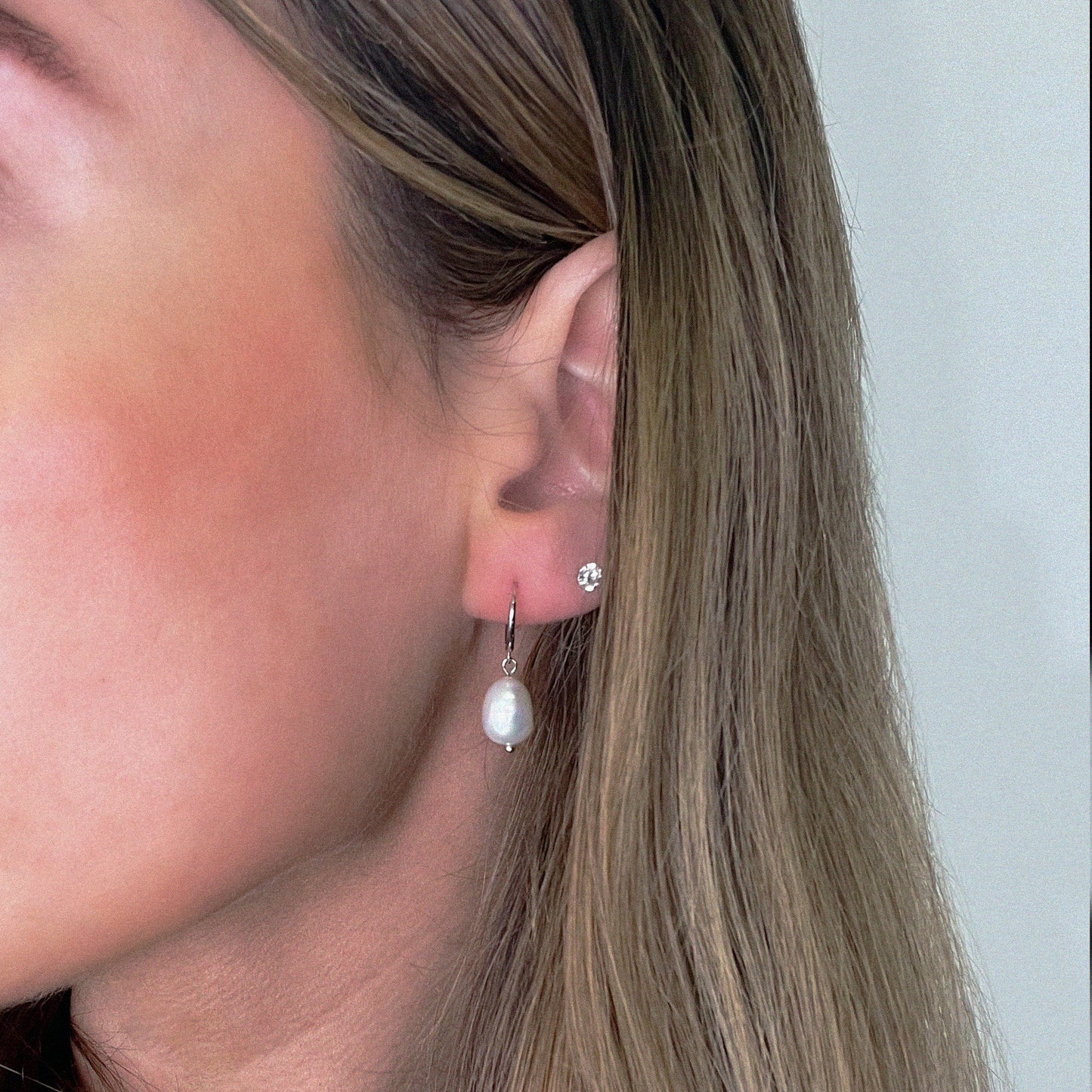 Close-up of an ear wearing pearl earrings with a neutral background