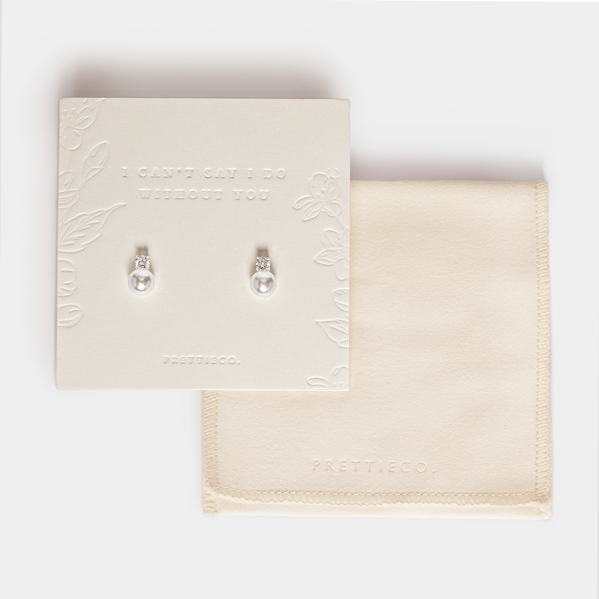 A pair of silver pearl earrings displayed on a cream-colored card, with a matching cream fabric pouch underneath on a light gray background. The card features embossed floral details and the text 'I CAN'T SAY I DO WITHOUT YOU'. Perfect for bridesmaid and bridal party gifting