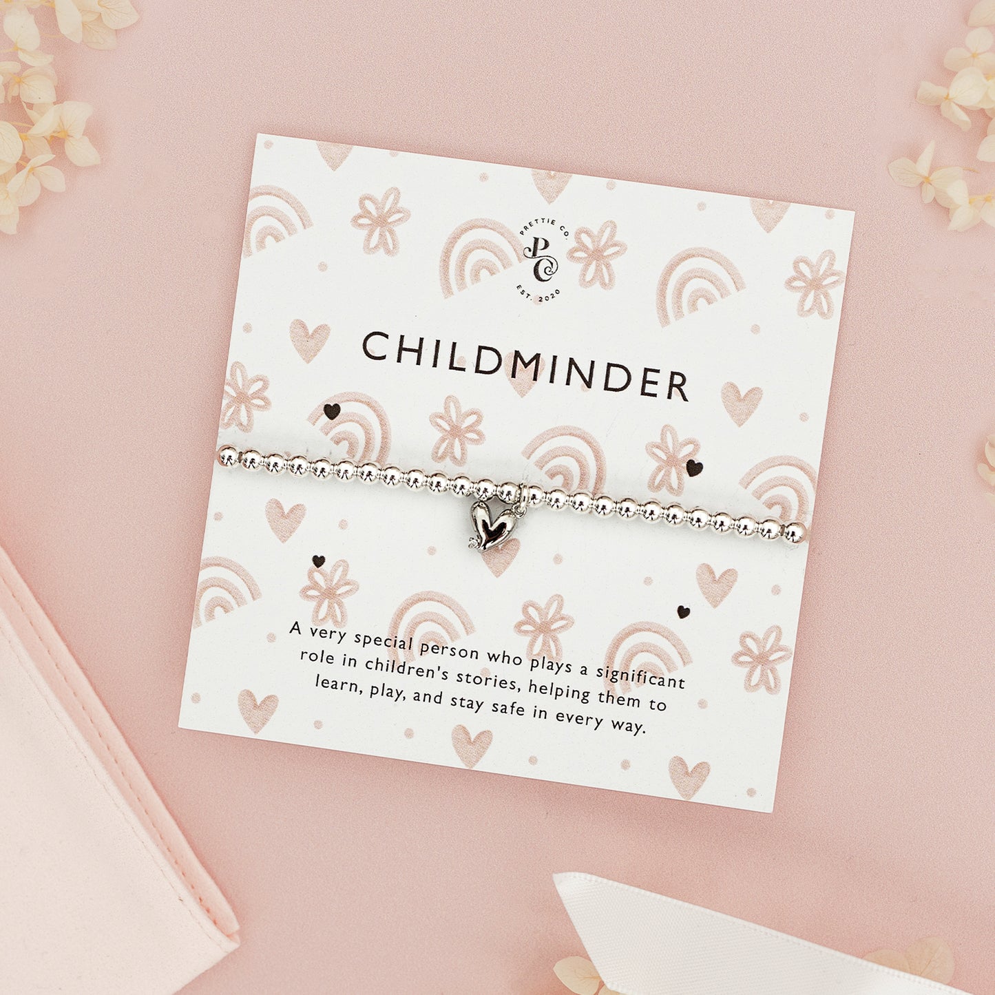 Personalised silver beaded bracelet with a heart charm for childmider, displayed on a custom card with heart illustrations, set against a pink background.