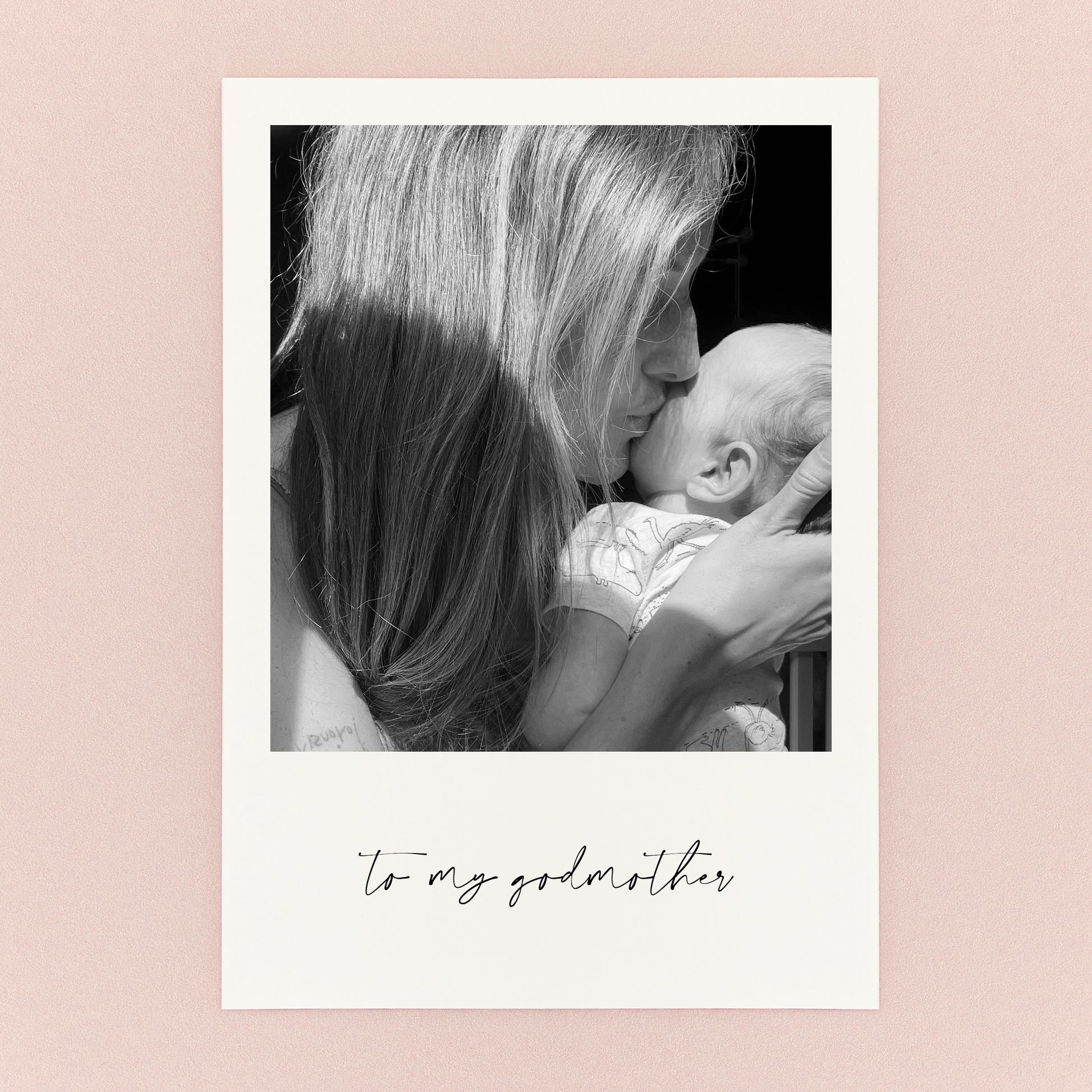 Black and white photo of a woman kissing a baby with 'To my godmother' text on a pink background