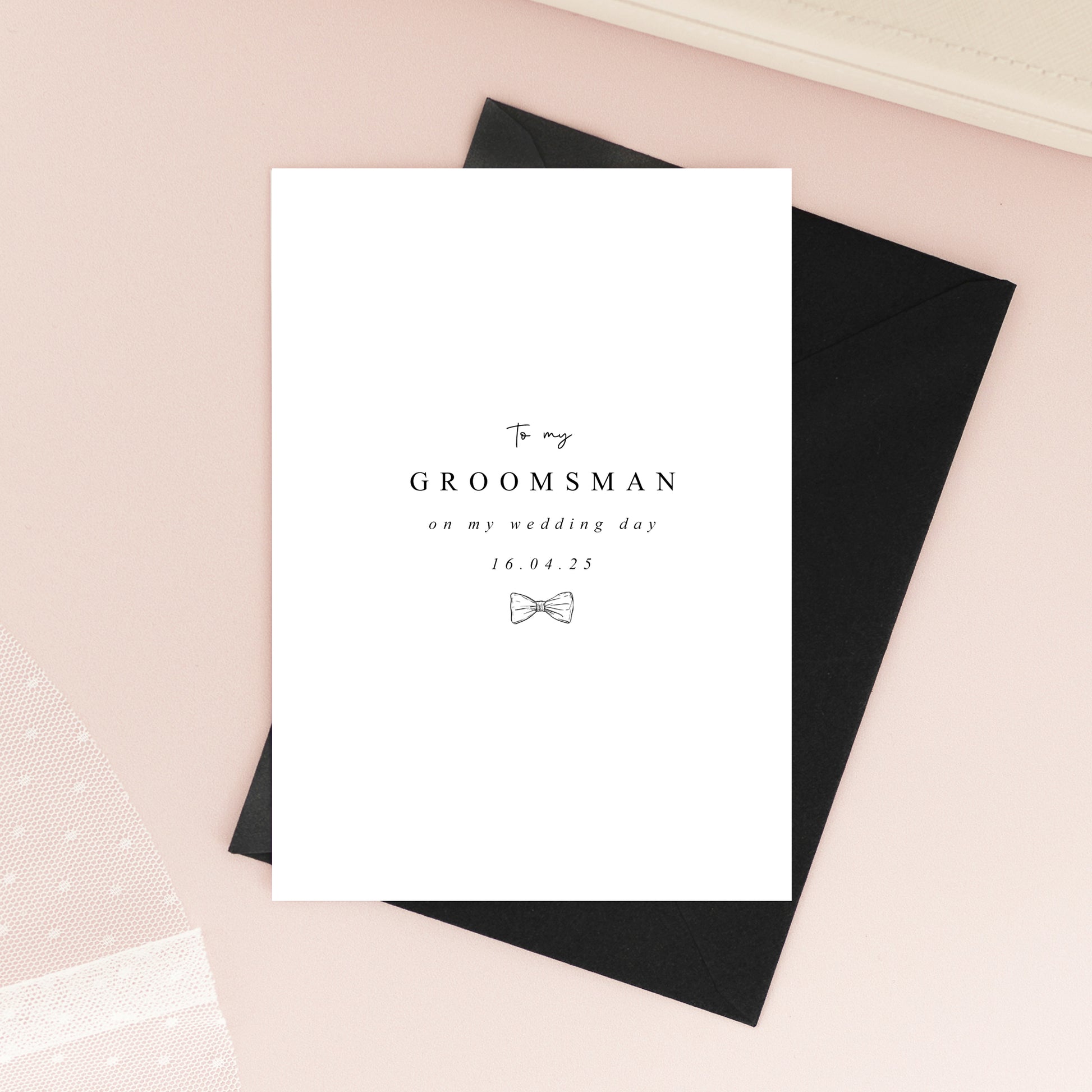 Folded A6 groomsmen card printed on textured white cardstock with a minimalist black bow tie illustration and elegant typography.
