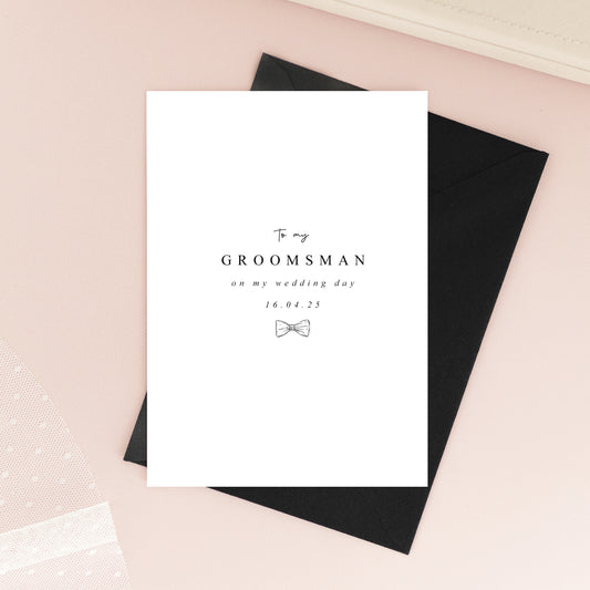 Folded A6 groomsmen card printed on textured white cardstock with a minimalist black bow tie illustration and elegant typography.
