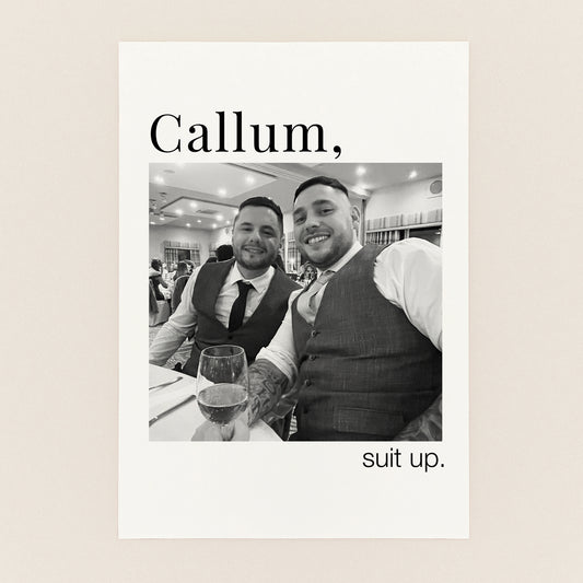 A personalized black and white wedding print featuring a photo of two men in suits, with the text 'Callum,' at the top and 'suit up.' at the bottom, displayed on a light beige background.