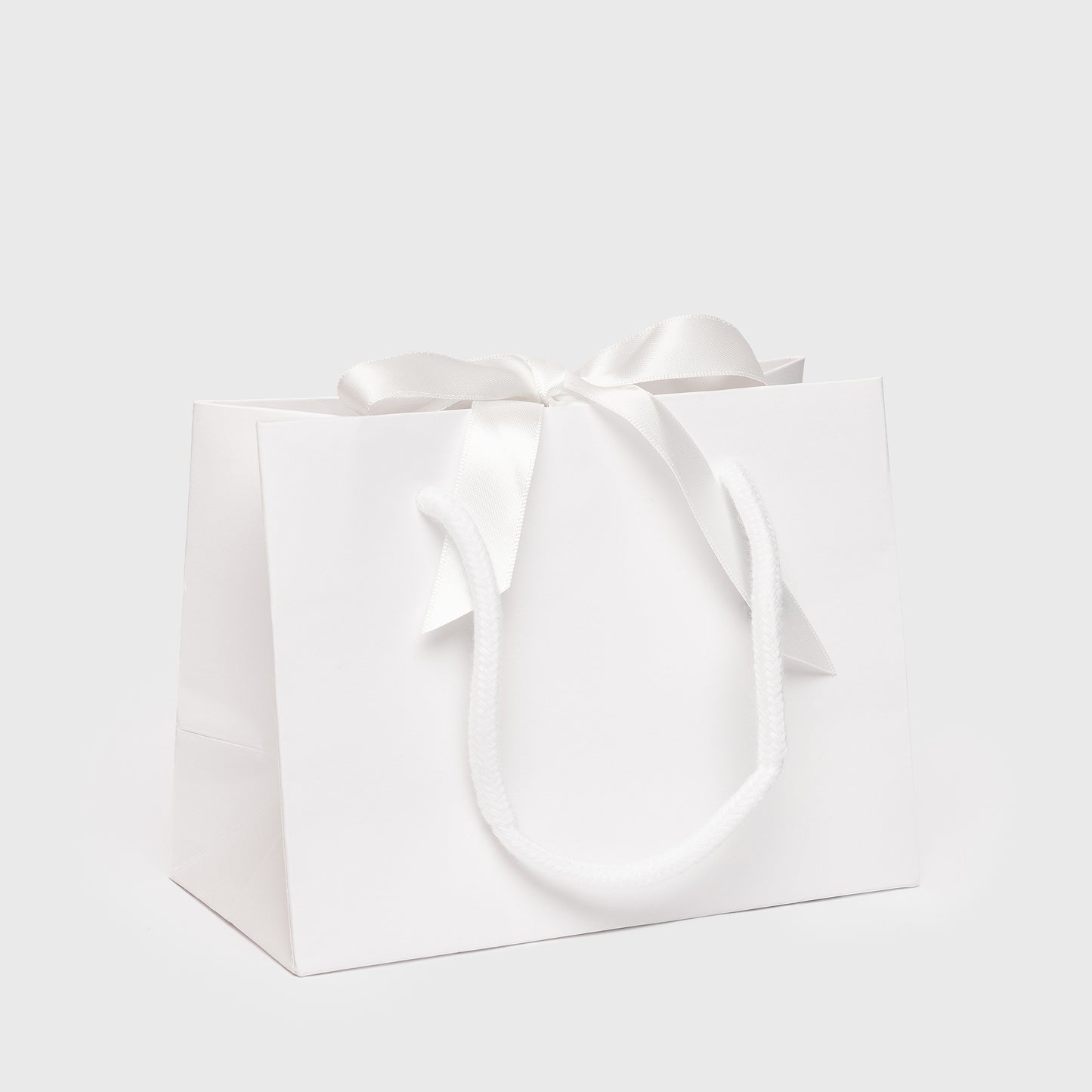 White gift bag with a bow on a light gray background