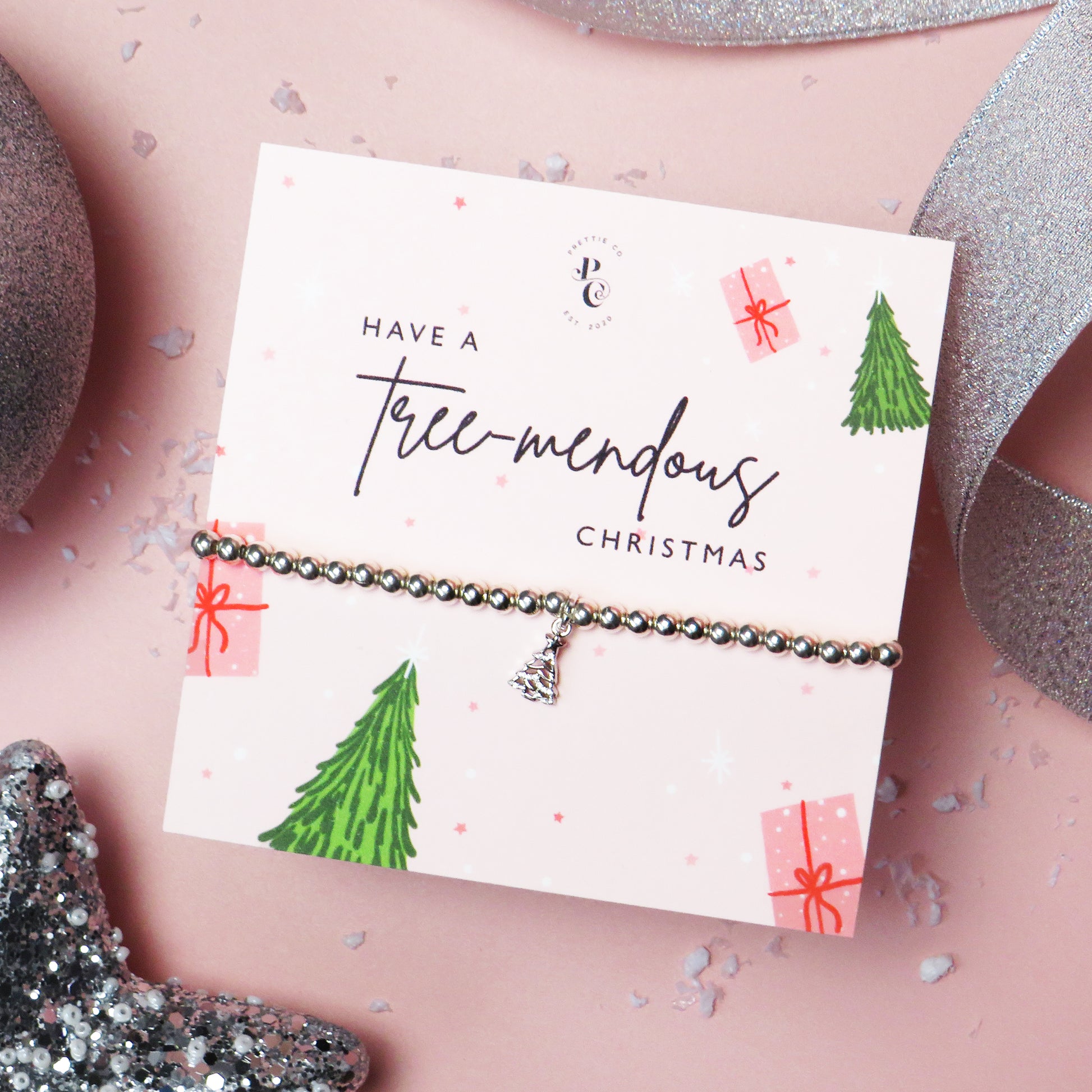 Silver-plated Christmas tree charm bracelet on a festive "Tree-mendous Christmas" card with holiday tree and gift illustrations, ideal for Christmas gifts and stocking fillers.